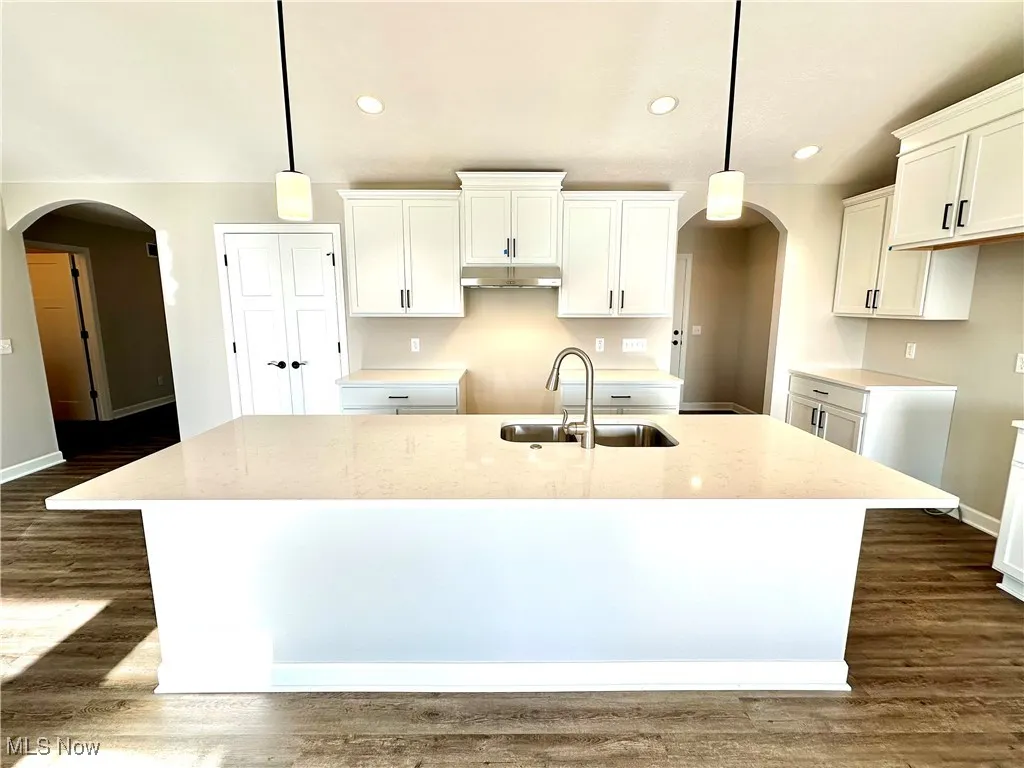 Kitchen with decorative light fixtures, a center island with sink, white cabinetry, and sink