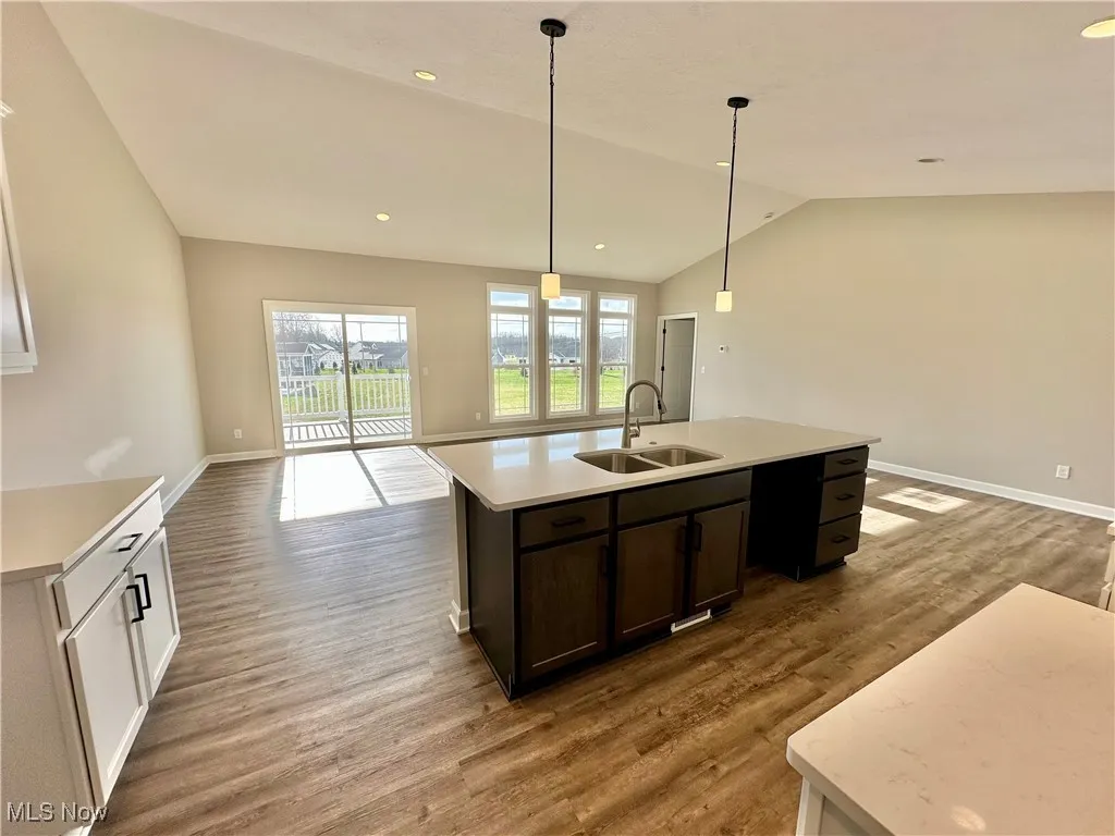 Kitchen featuring sink, decorative light fixtures, hardwood / wood-style flooring, a center island with sink, and lofted ceiling