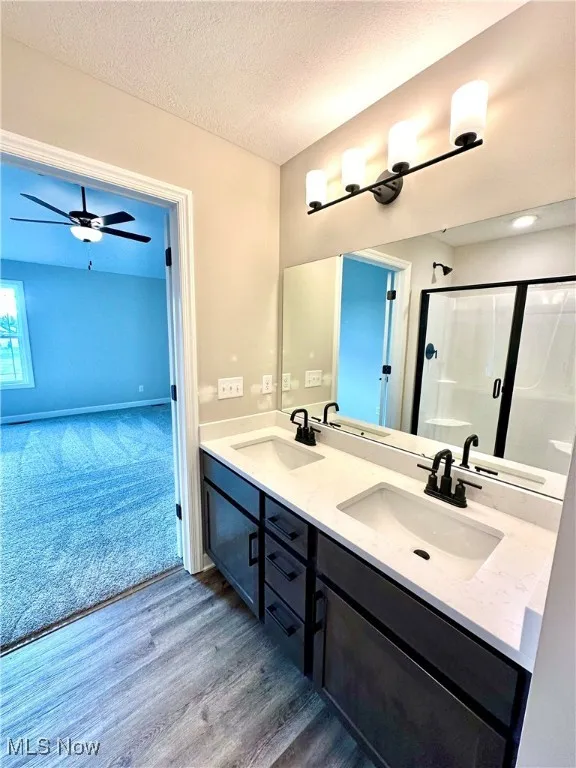 Bathroom featuring vanity, ceiling fan, a textured ceiling, walk in shower, and wood-type flooring