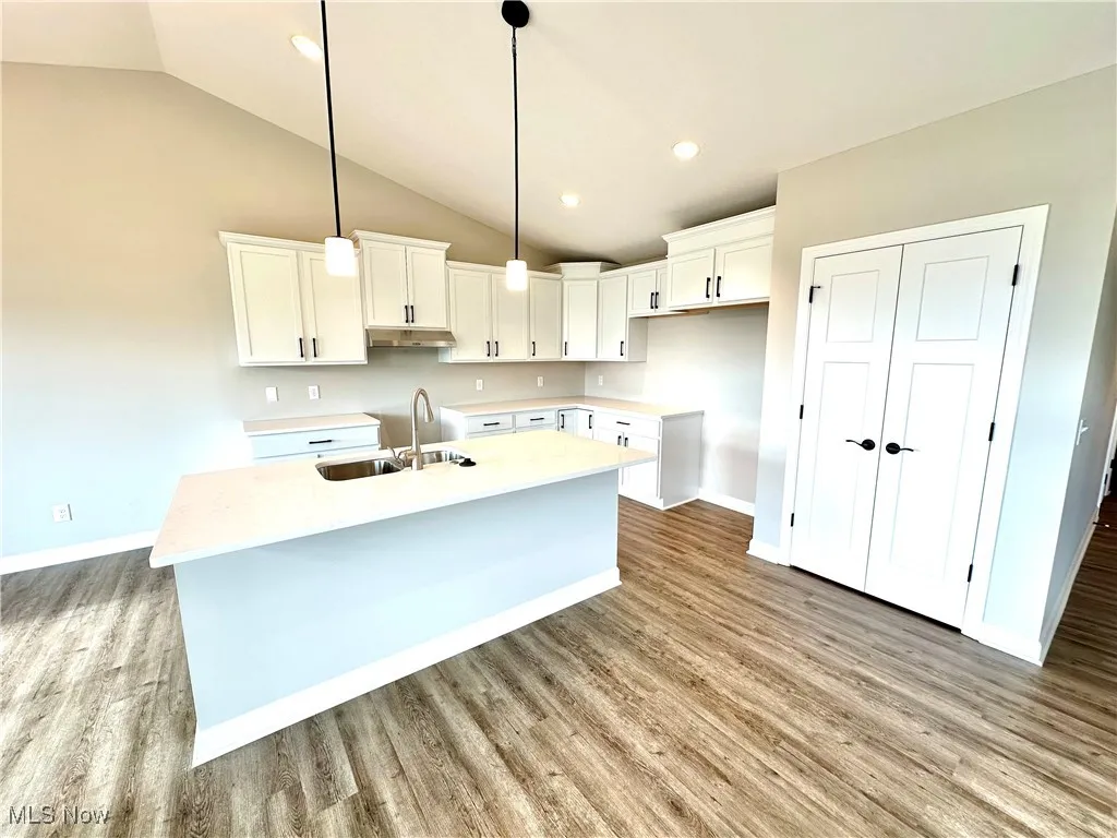 Kitchen with a center island with sink, sink, vaulted ceiling, decorative light fixtures, and white cabinetry