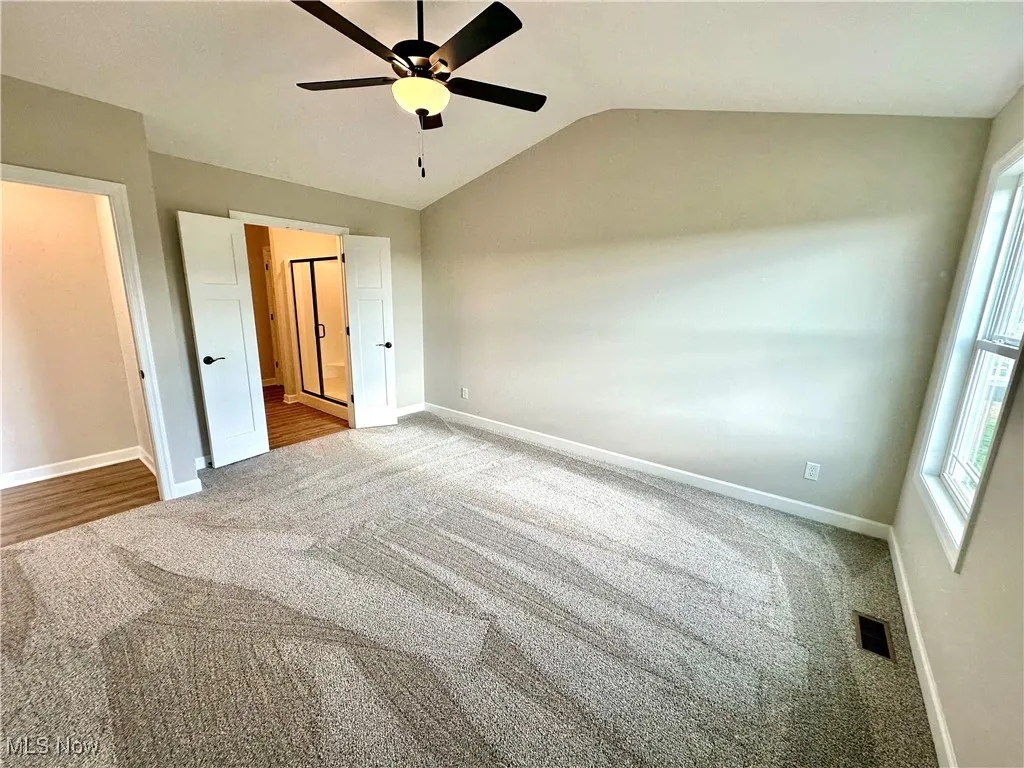 Unfurnished bedroom featuring ceiling fan, light carpet, and vaulted ceiling