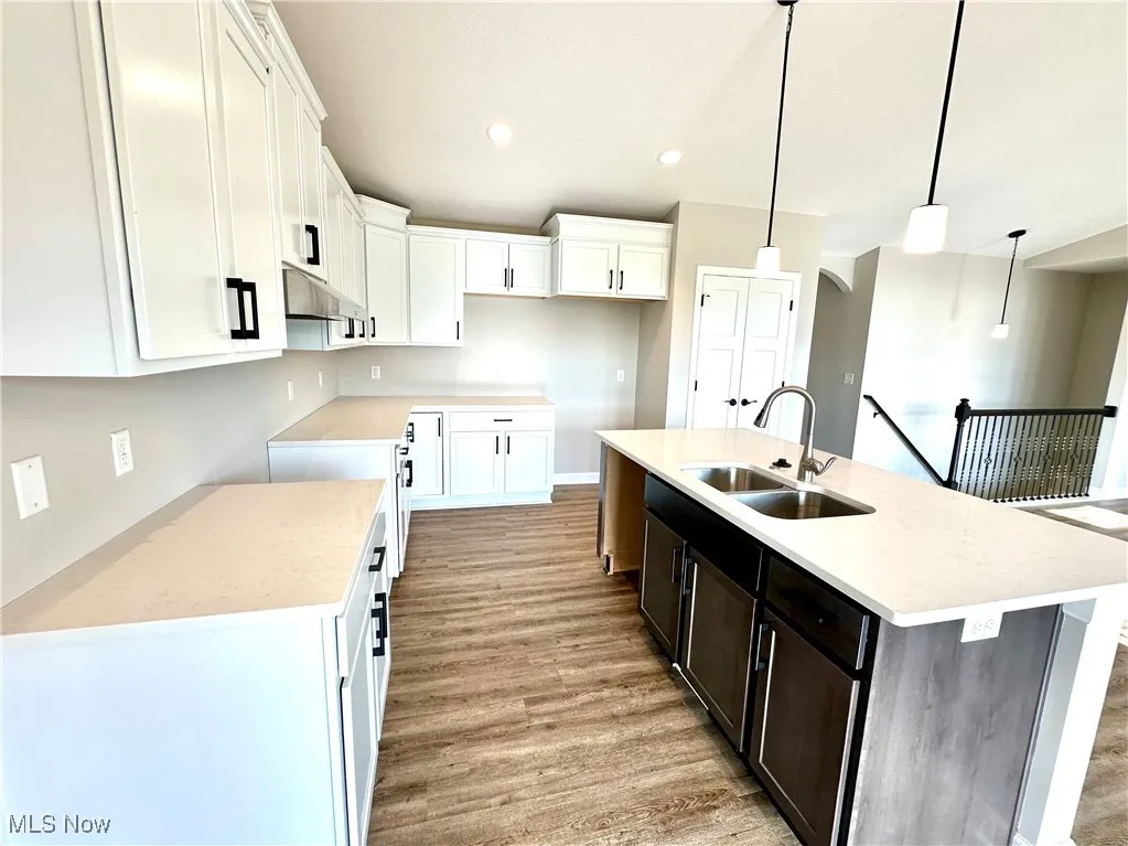 Kitchen with white cabinetry, sink, an island with sink, and decorative light fixtures
