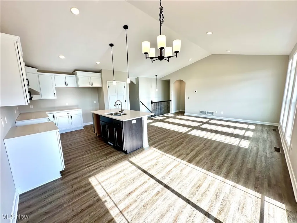 Kitchen with a kitchen island with sink, sink, decorative light fixtures, white cabinets, and lofted ceiling