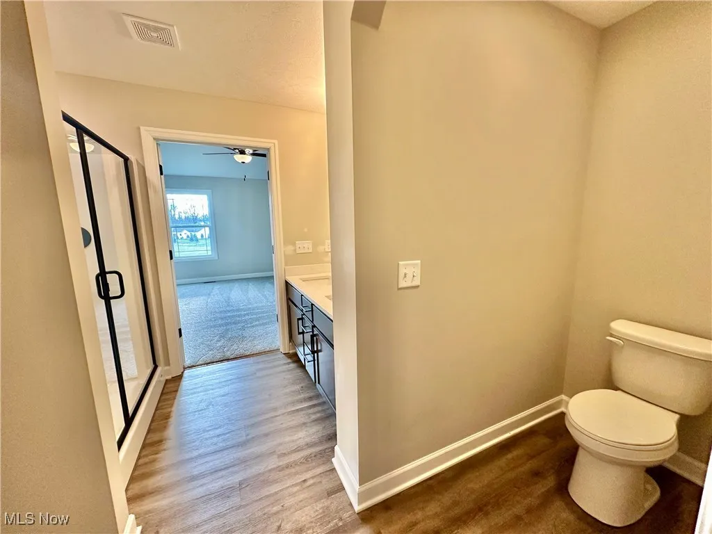 Bathroom featuring ceiling fan, wood-type flooring, toilet, vanity, and a shower with shower door