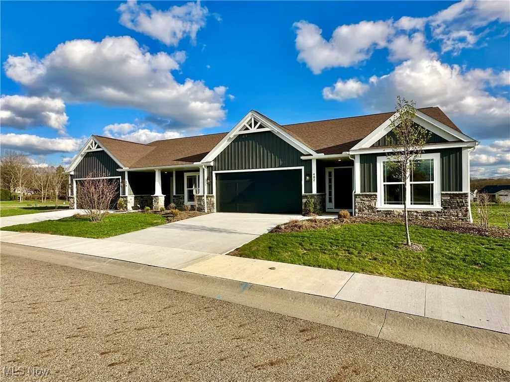 Craftsman-style home with an attached garage, stone siding, concrete driveway, a front lawn, and roof with shingles