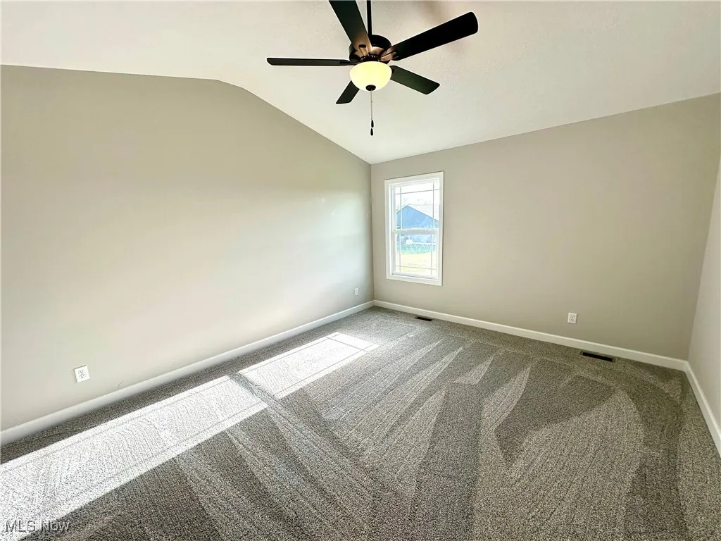 Carpeted empty room featuring vaulted ceiling and ceiling fan