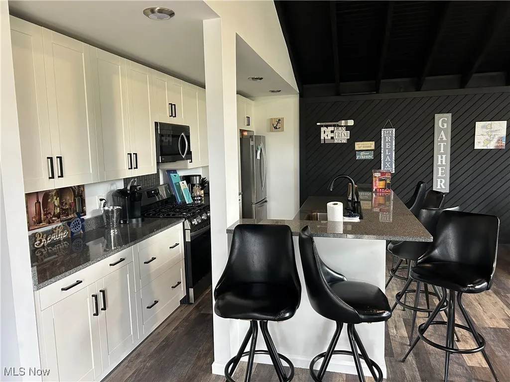 Kitchen featuring sink, dark hardwood / wood-style flooring, a breakfast bar, white cabinets, and appliances with stainless steel finishes