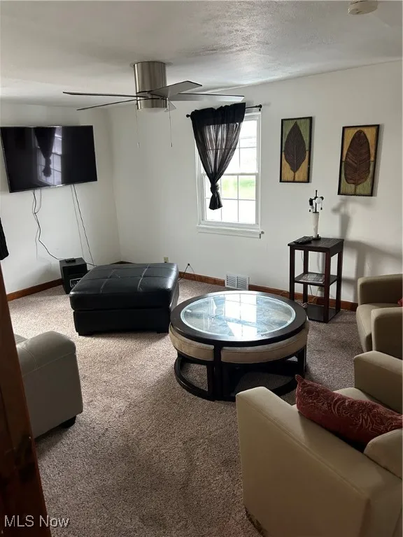 Carpeted living room with ceiling fan and a textured ceiling