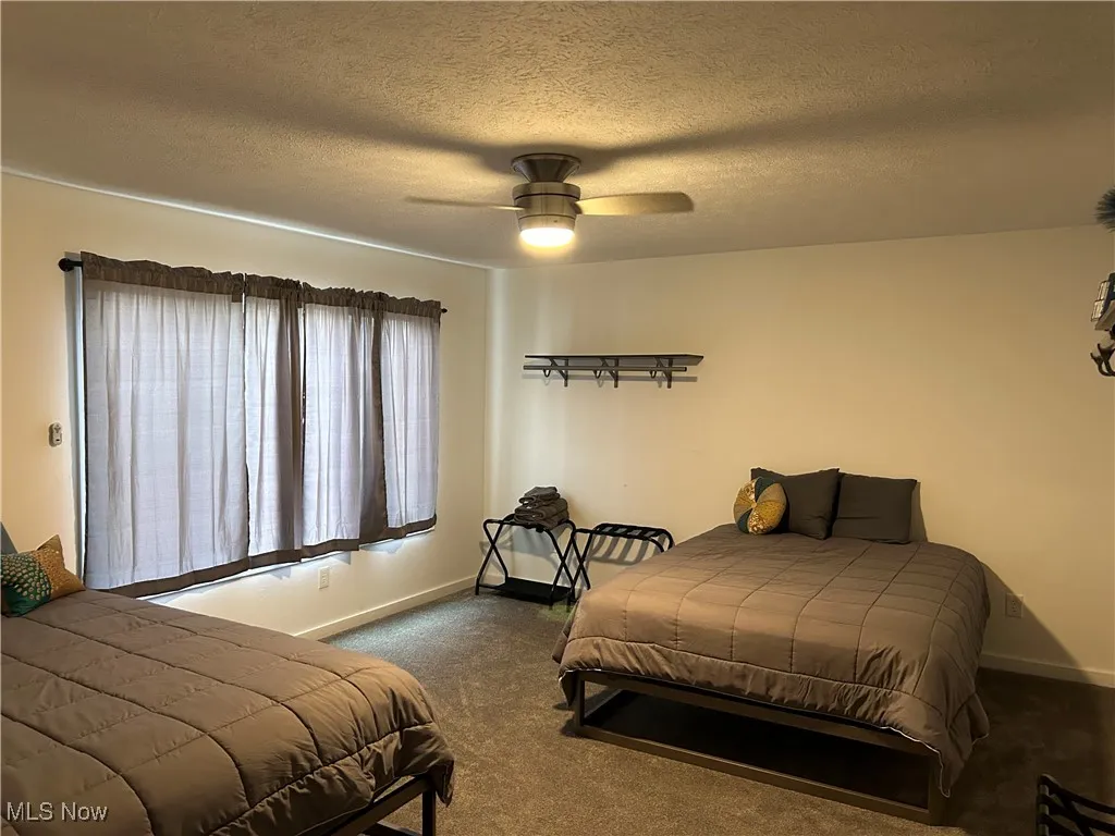 Bedroom featuring a textured ceiling, dark carpet, and ceiling fan