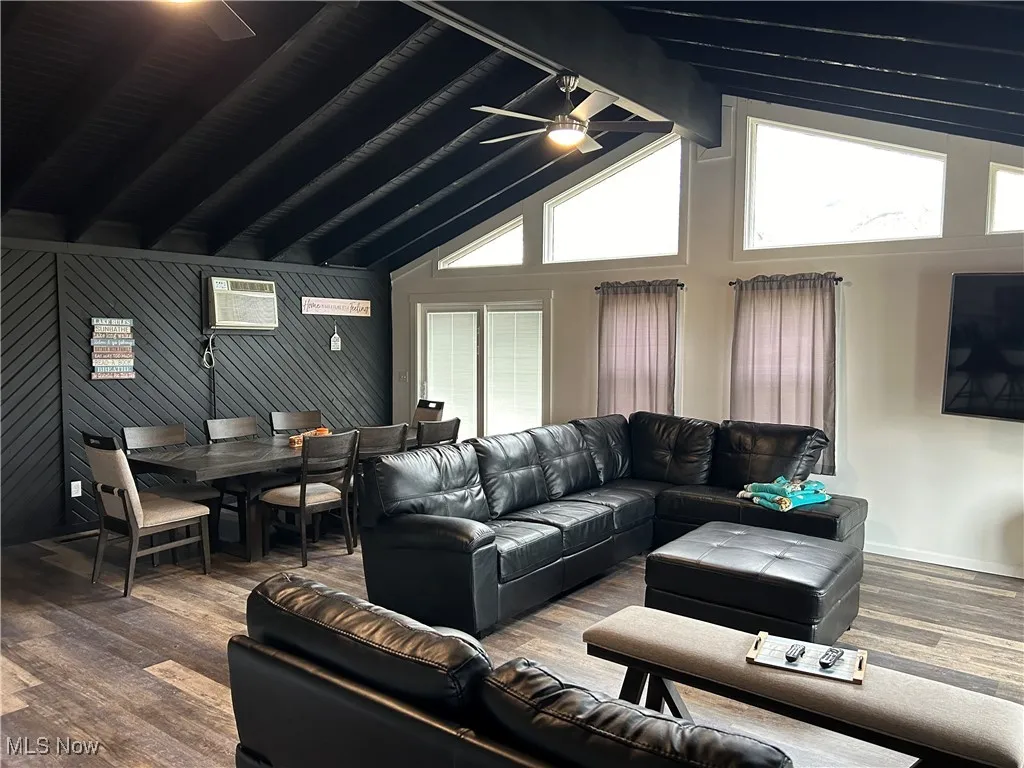 Living room featuring a wall mounted air conditioner, ceiling fan, beam ceiling, high vaulted ceiling, and hardwood / wood-style floors