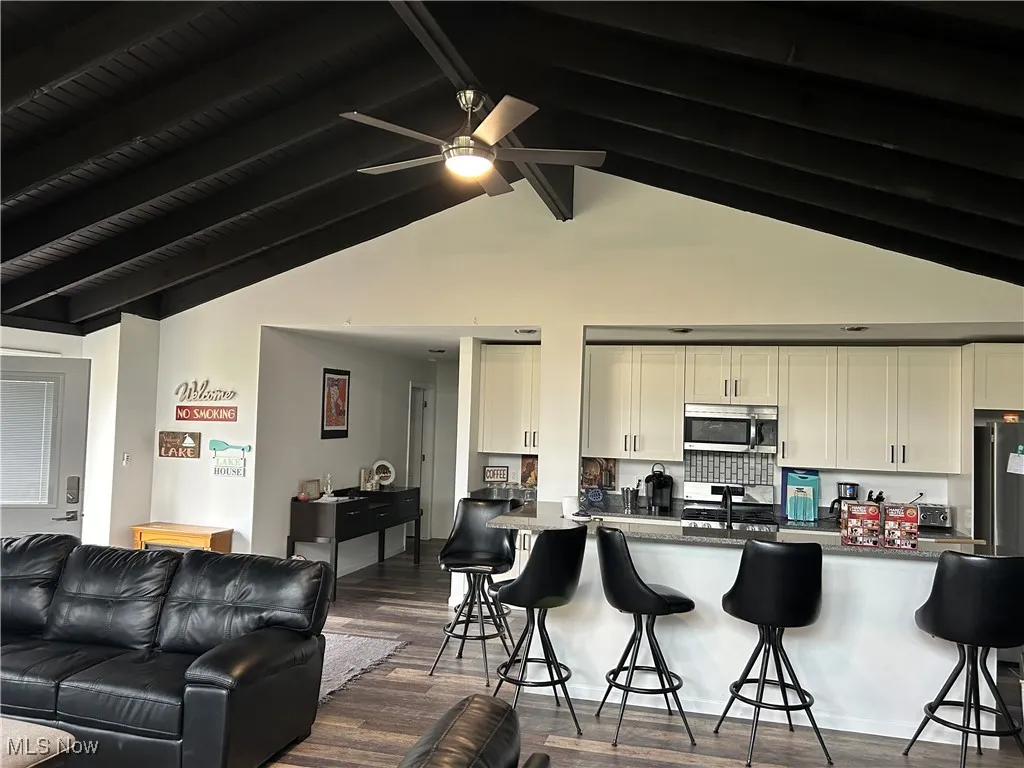 Kitchen featuring a kitchen bar, stainless steel appliances, dark wood-type flooring, high vaulted ceiling, and beamed ceiling