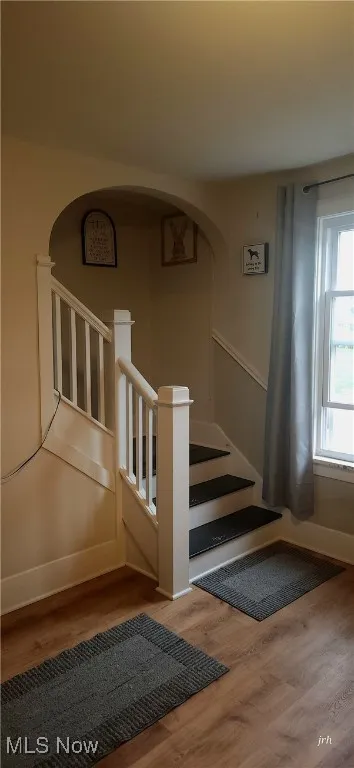 Staircase featuring arched walkways, wood finished floors, and baseboards
