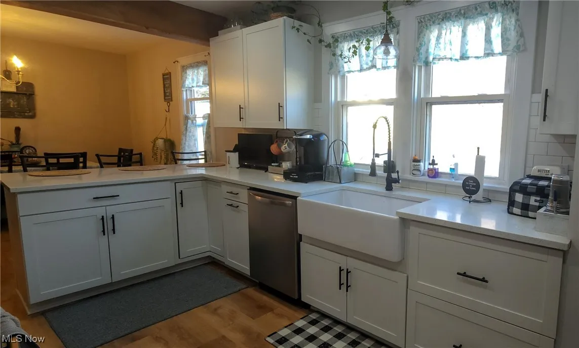 Kitchen featuring apron sink, shaker cabinets, quartz countertops, dishwasher, laminate flooring.