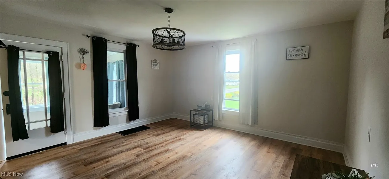 Unfurnished dining area featuring a chandelier, healthy amount of natural light, wood finished floors, and baseboards