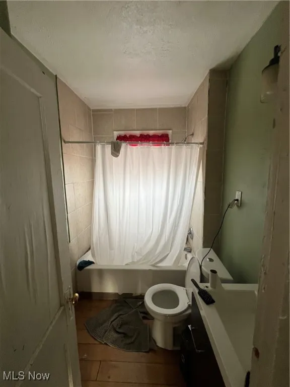 Bathroom with shower / tub combo, a textured ceiling, toilet, and wood-type flooring
