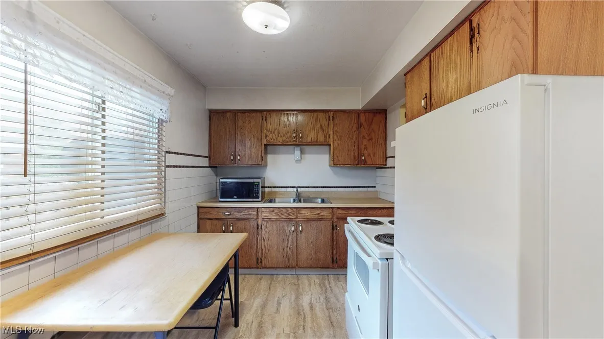Kitchen featuring tasteful backsplash, light hardwood / wood-style flooring, white appliances, and sink