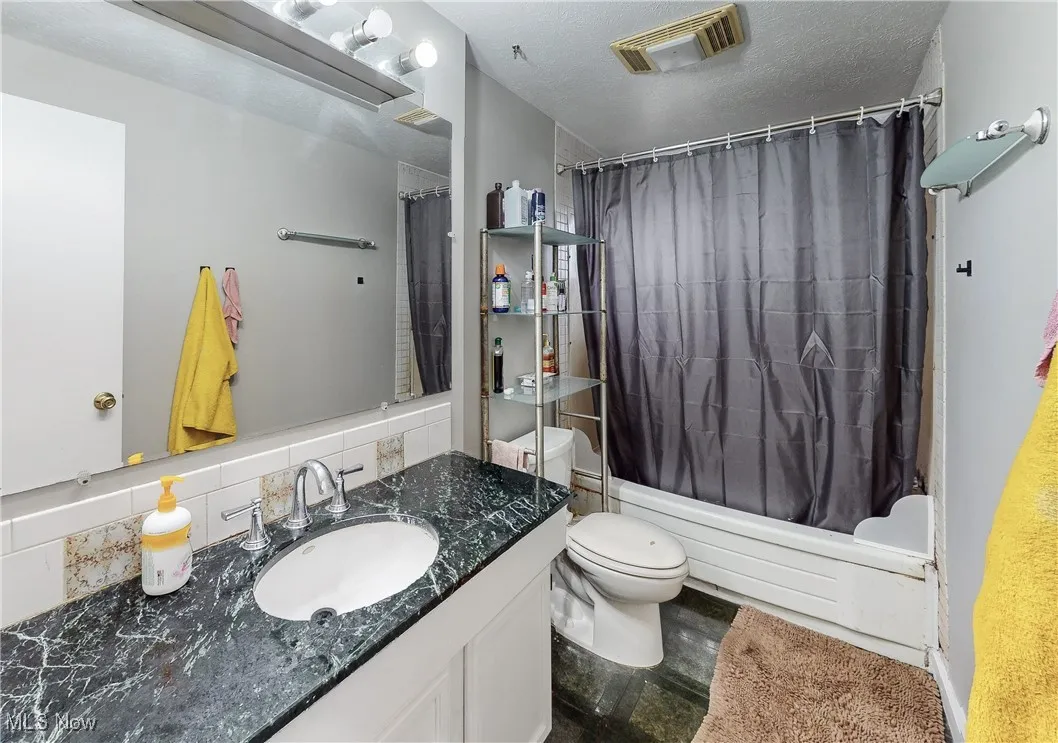 Full bathroom with tasteful backsplash, shower / bathtub combination with curtain, a textured ceiling, and toilet