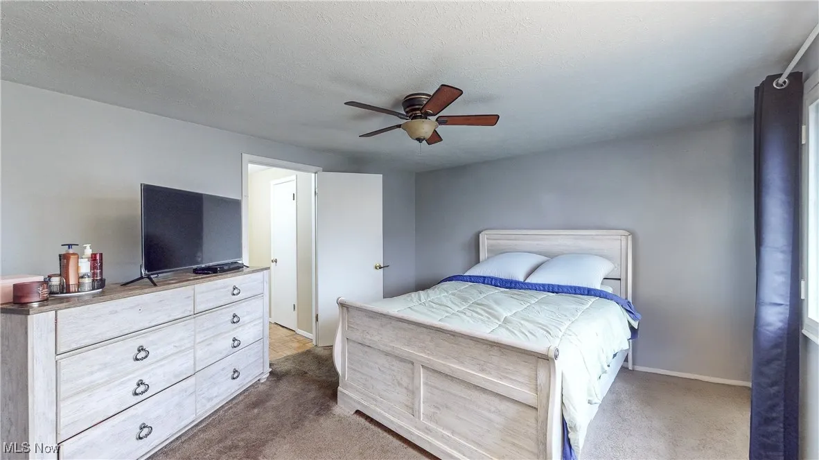 Bedroom with ceiling fan, dark carpet, and a textured ceiling