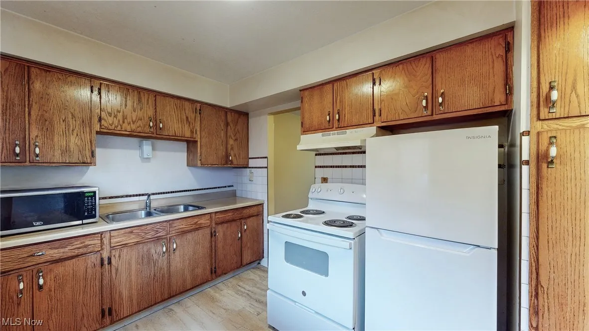 Kitchen featuring decorative backsplash, sink, white appliances, and light hardwood / wood-style flooring