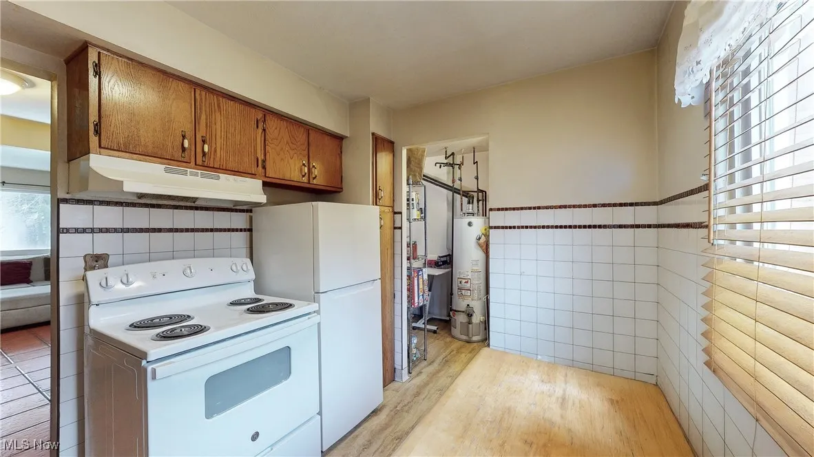 Kitchen featuring gas water heater, white appliances, light hardwood / wood-style floors, and tile walls