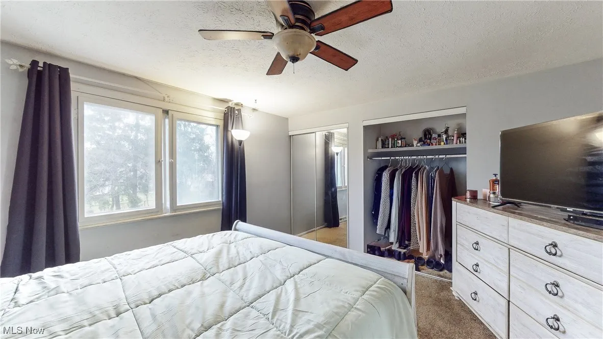Carpeted bedroom featuring ceiling fan and a textured ceiling