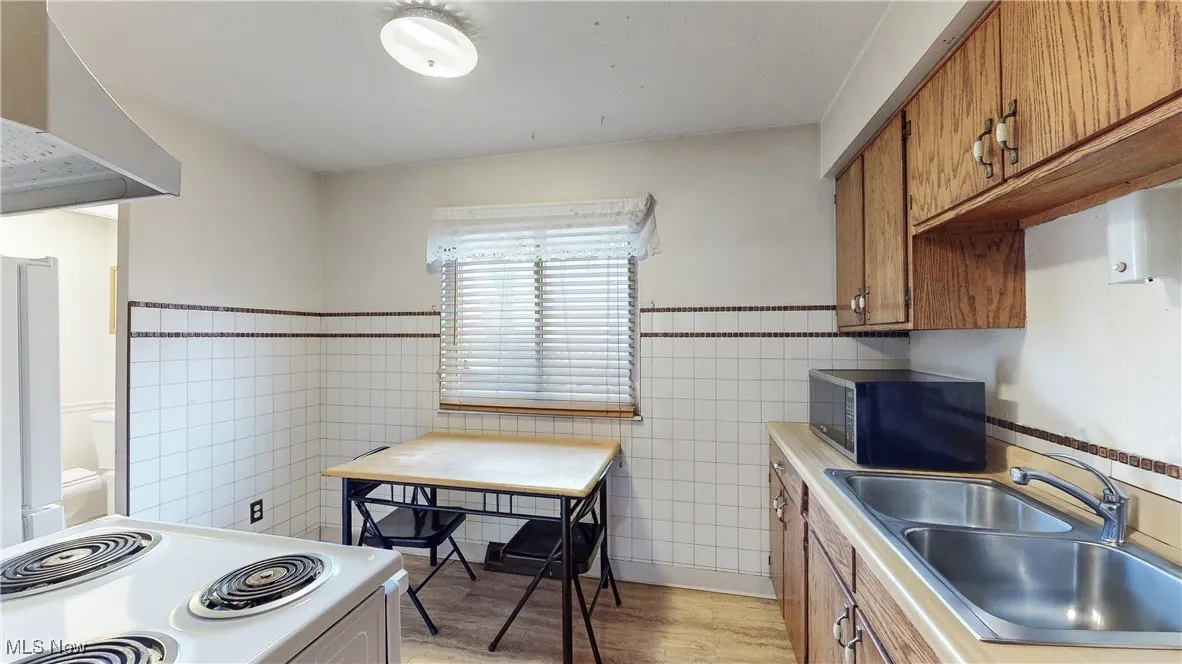 Kitchen featuring white range, light hardwood / wood-style flooring, tile walls, and sink