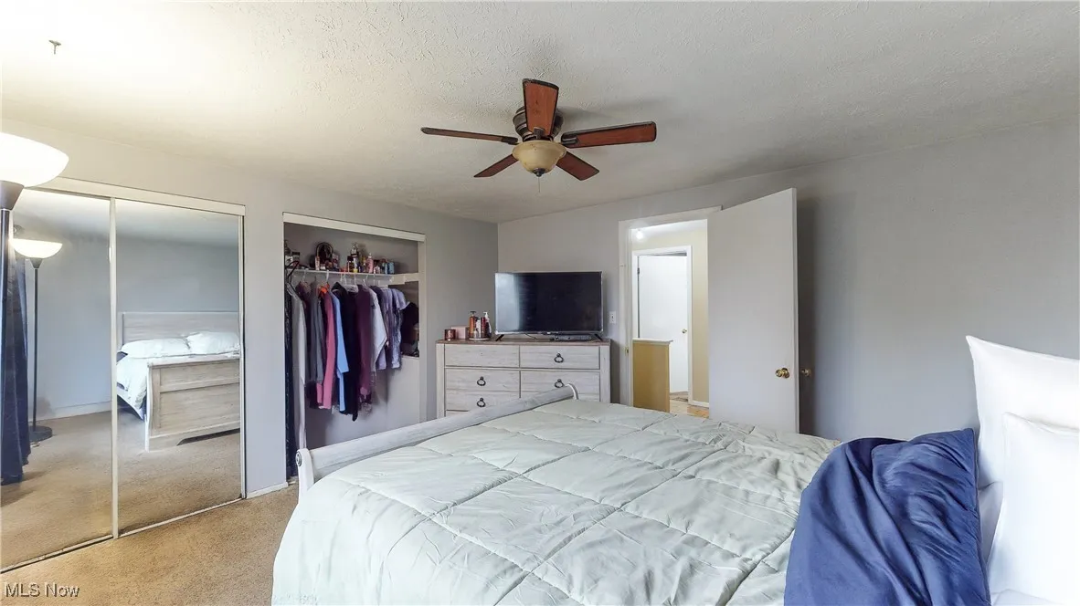Bedroom featuring multiple closets, ceiling fan, light carpet, and a textured ceiling