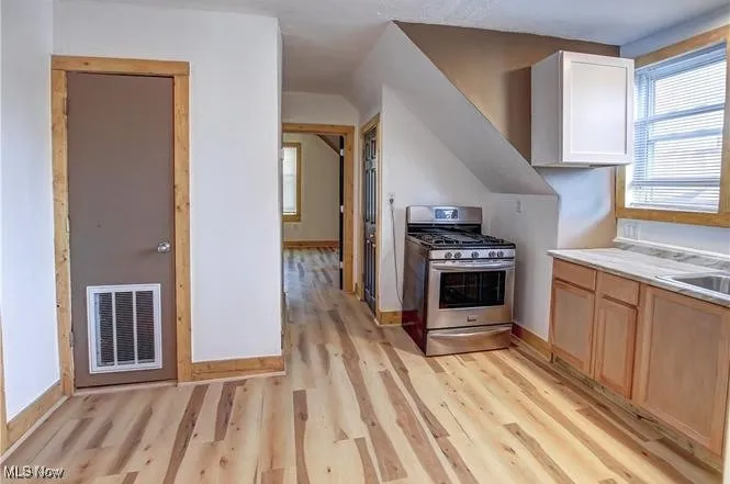 Kitchen with gas stove, light hardwood / wood-style flooring, and white cabinets