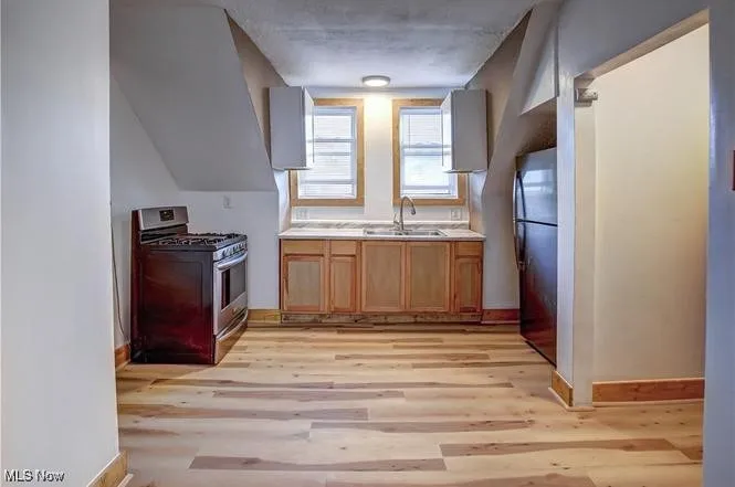 Kitchen with light wood-type flooring, gas stove, refrigerator, and sink