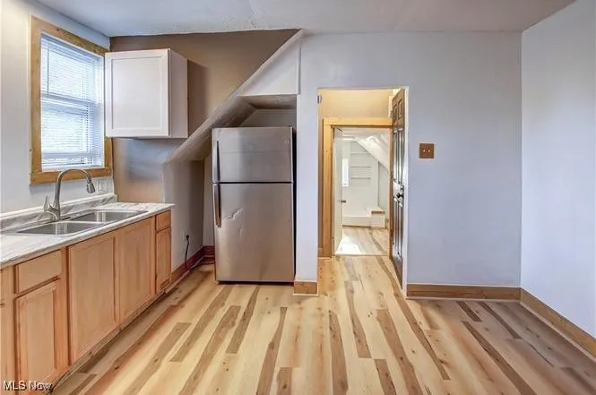 Kitchen featuring white cabinets, light hardwood / wood-style flooring, stainless steel refrigerator, and sink