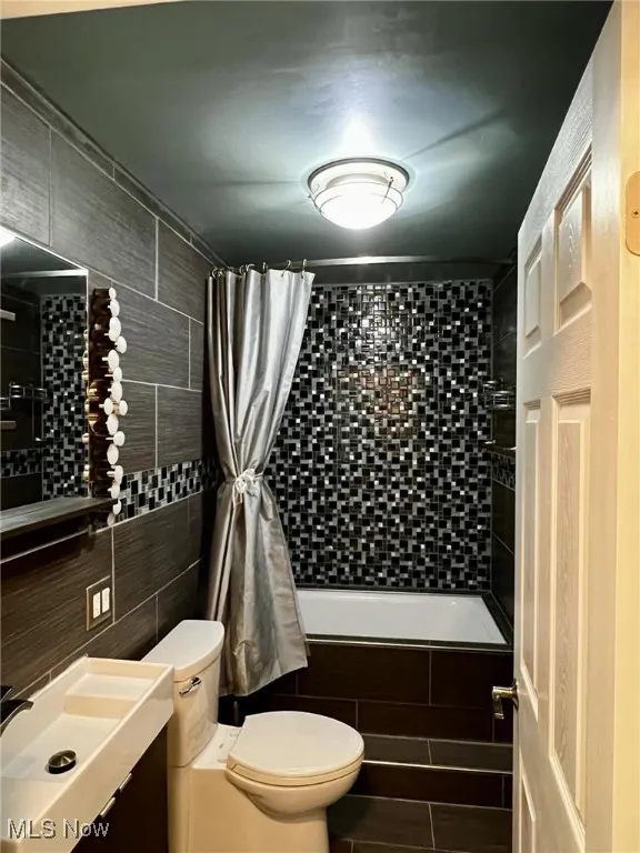 Full bathroom featuring shower / bath combo, toilet, tile walls, and vanity