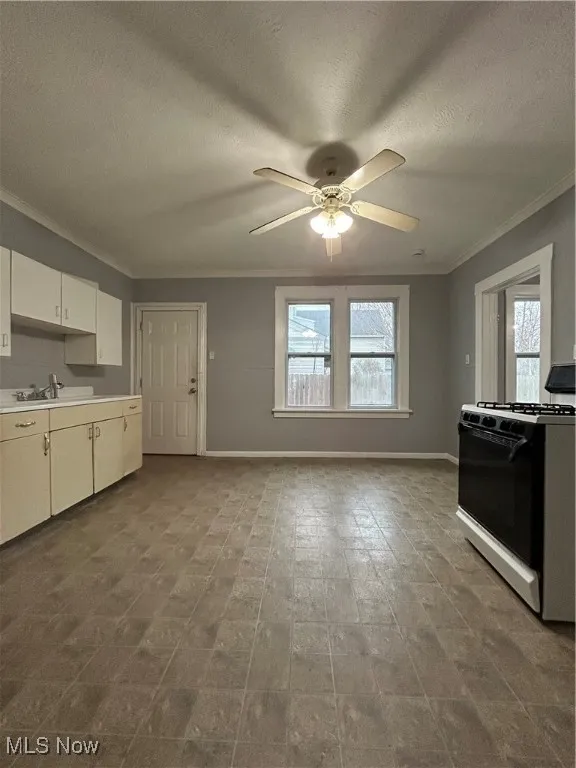 Kitchen with ceiling fan, crown molding, sink, white cabinets, and range