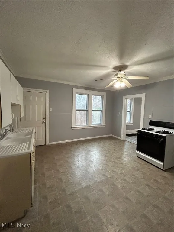 Kitchen with white cabinets, range, ceiling fan, and crown molding