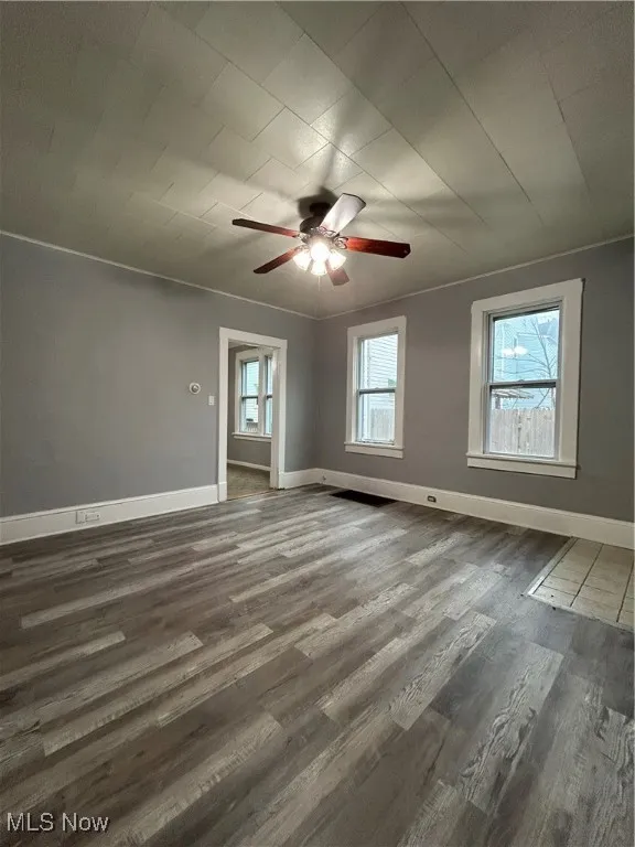Spare room with dark hardwood / wood-style floors, ceiling fan, ornamental molding, and a wealth of natural light