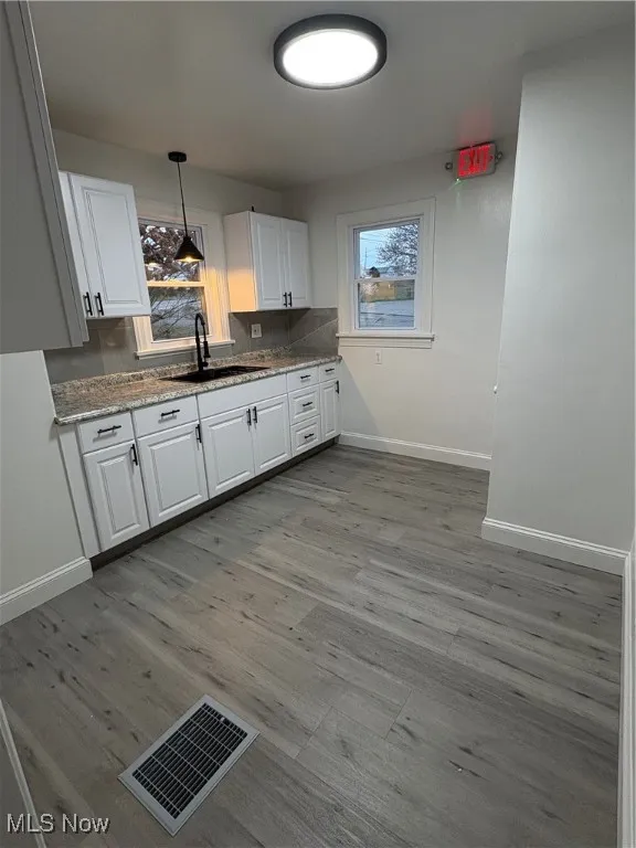 Kitchen featuring backsplash, light stone counters, sink, white cabinets, and hanging light fixtures