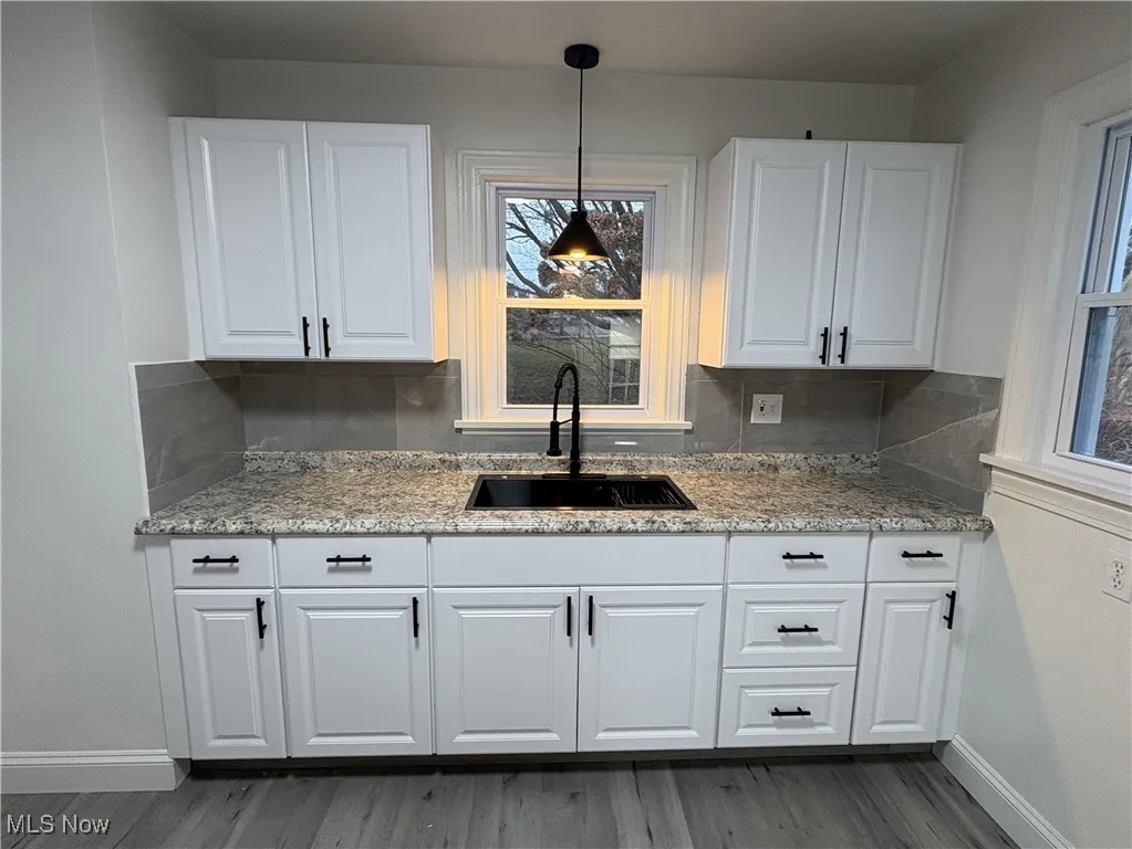 Kitchen featuring pendant lighting, backsplash, sink, light stone countertops, and white cabinetry