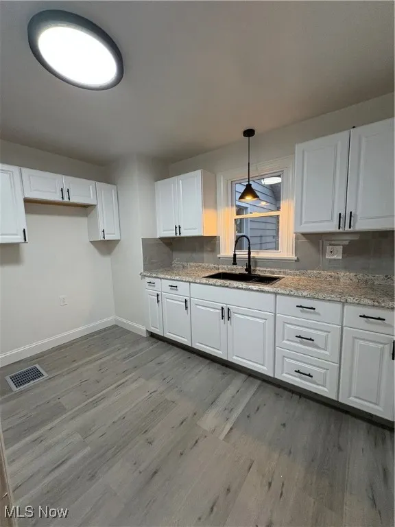 Kitchen featuring light stone counters, sink, light hardwood / wood-style floors, white cabinetry, and hanging light fixtures