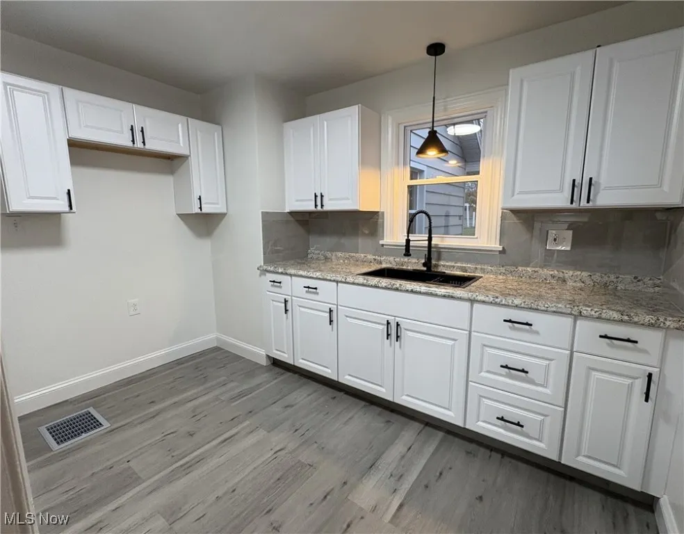 Kitchen featuring white cabinets, decorative backsplash, pendant lighting, and sink
