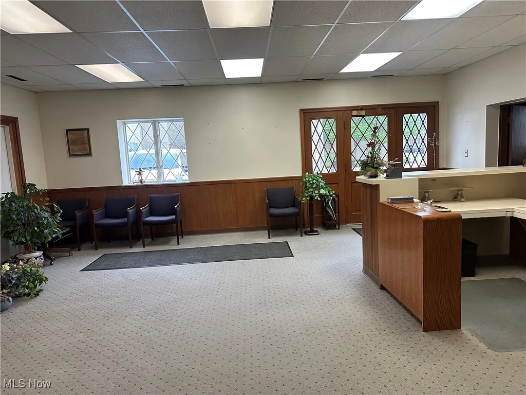 Home office with light carpet, a drop ceiling, wainscoting, and wooden walls