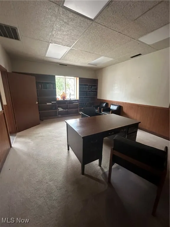 Carpeted home office with a wainscoted wall, a paneled ceiling, and wooden walls
