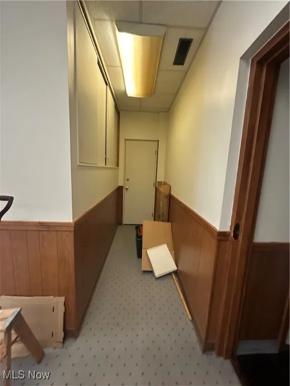 Corridor featuring a wainscoted wall, wood walls, and a drop ceiling