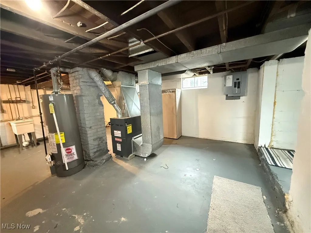 Below grade area with water heater, electric panel, heating unit, and a sink