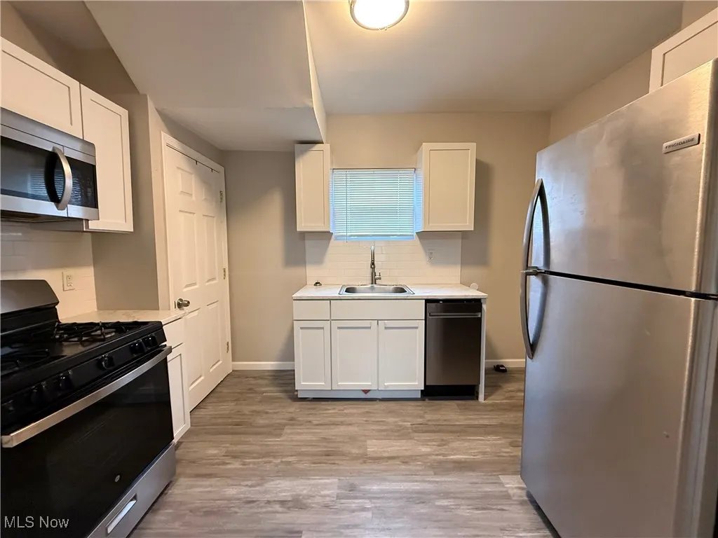Kitchen with white cabinetry, light countertops, a sink, and stainless steel appliances