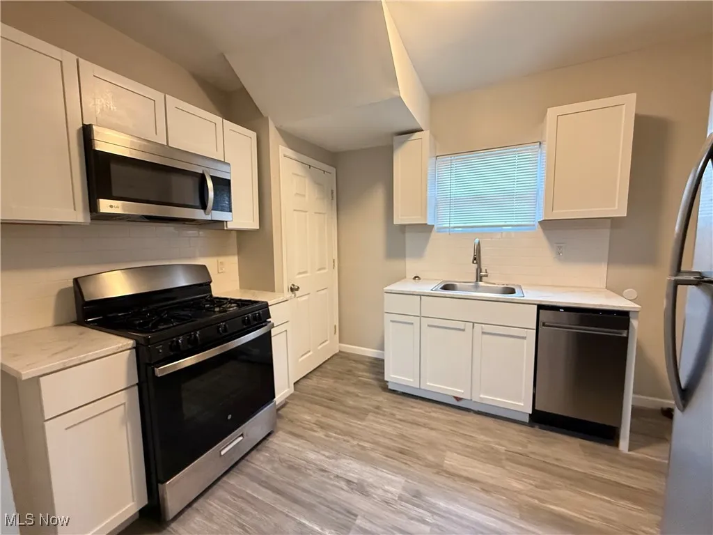 Kitchen with a sink, white cabinetry, light countertops, and appliances with stainless steel finishes