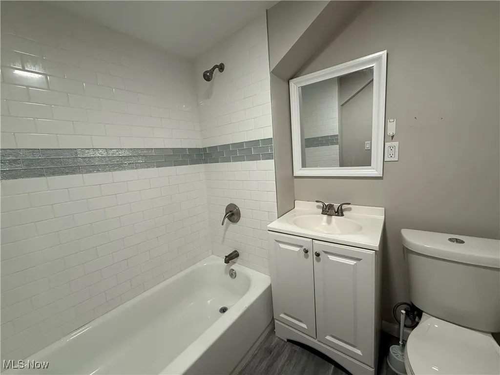 Full bathroom featuring wood finished floors, toilet, vanity, and washtub / shower combination