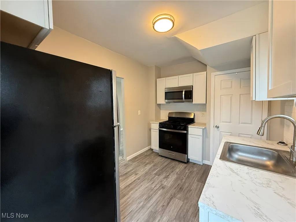 Kitchen with a sink, light wood finished floors, white cabinetry, stainless steel appliances, and baseboards