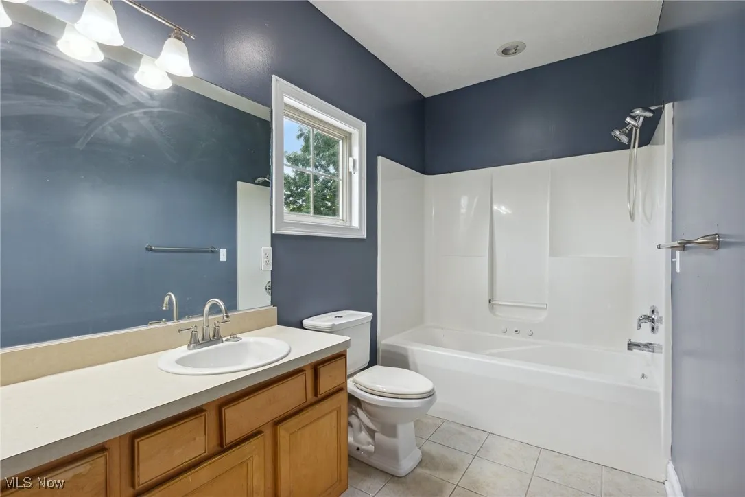 Full bathroom with tile patterned floors,  shower combination, vanity, and toilet