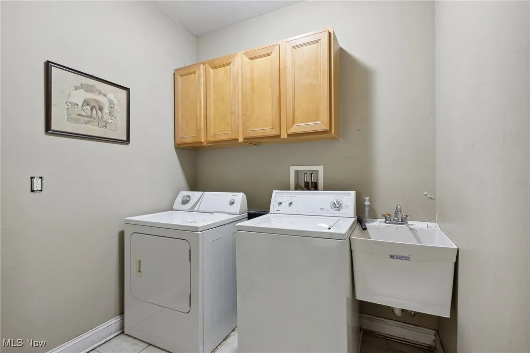 Clothes washing area with sink, washer and clothes dryer, cabinets, and light tile patterned floors
