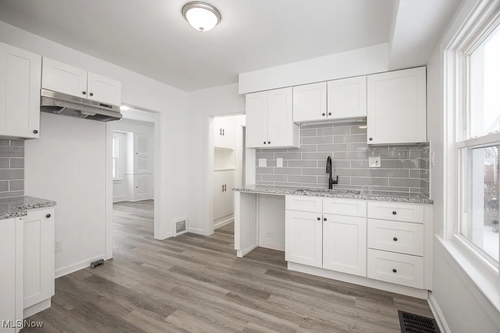 Kitchen with decorative backsplash, white cabinetry, and sink