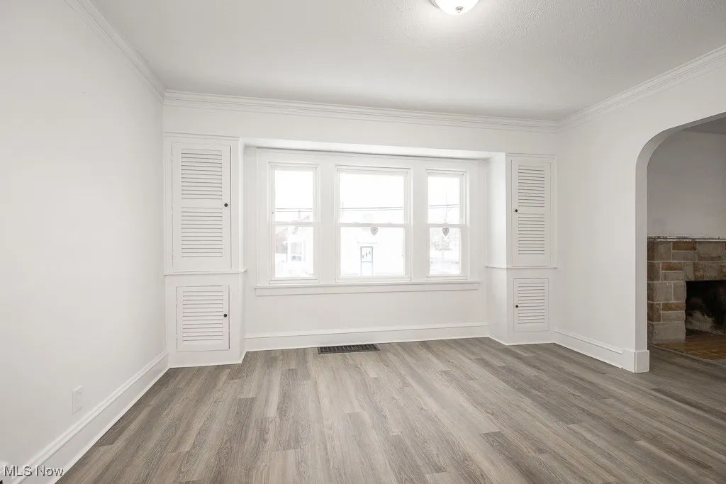 Empty room with hardwood / wood-style floors, a stone fireplace, and ornamental molding